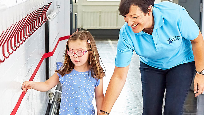 A little girl and a Guide Dogs support worker walking down a school corridor
